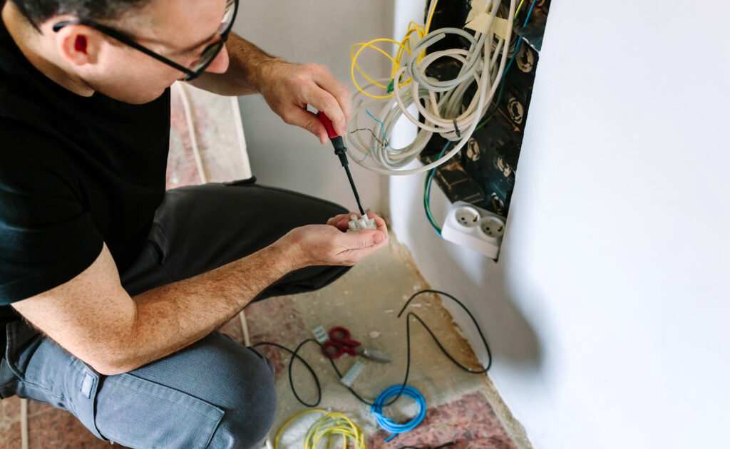 Male technician with screwdriver and terminal strip installing telecommunication box. Boca Electrical Services Boca Raton