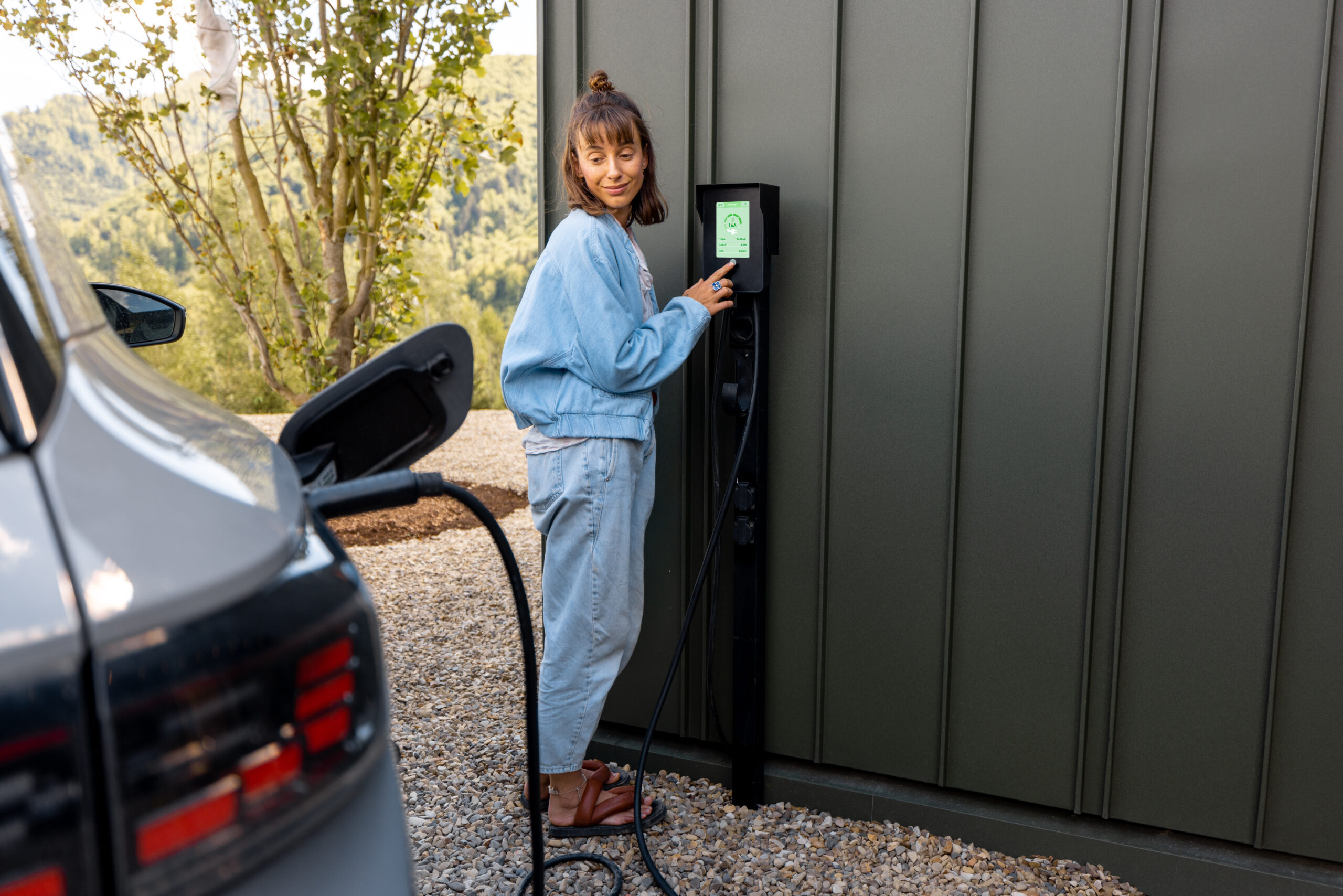 Woman switches on car charging station while charging her electric vehicle near home. Concept of smart technologies for comfort living, EV cars Boca Electrical Services Boca Raton