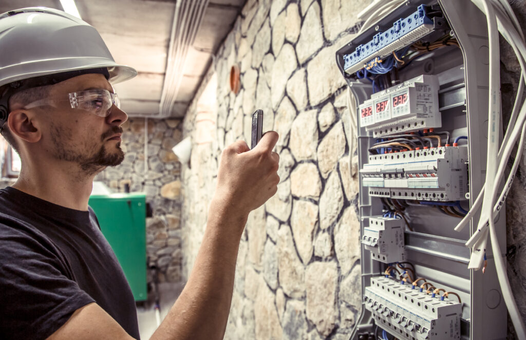 a male electrician works in a switchboard with an electrical connecting cable, connects the equipment with tools, the concept of complex work, space for text