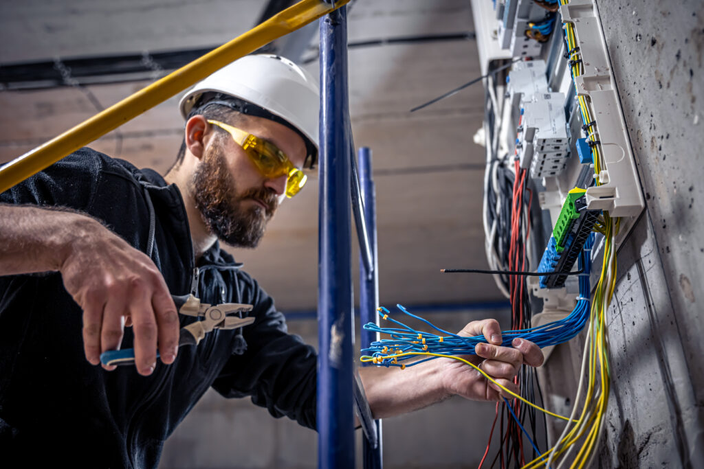 A male electrician works in a switchboard with an electrical connecting cable, connects the equipment with tools. Boca Electrical Services Boca Raton