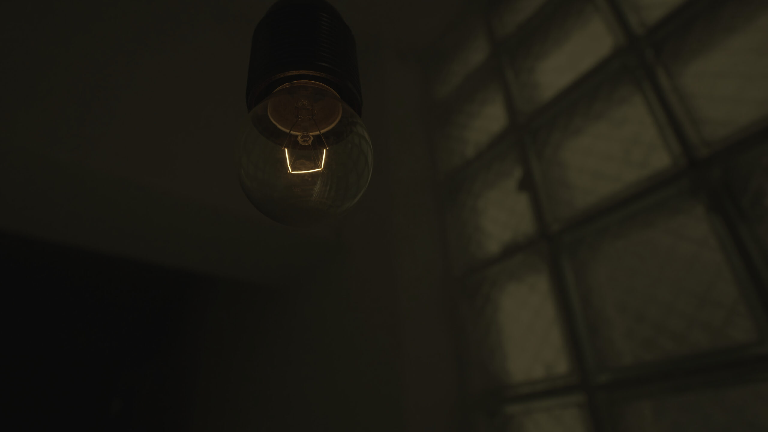 Bottom view of a hanging swaying light bulb inside the entrance of a buiulding. Close up of a blinking yellow light bulb in a dark and mystical atmosphere of a building.