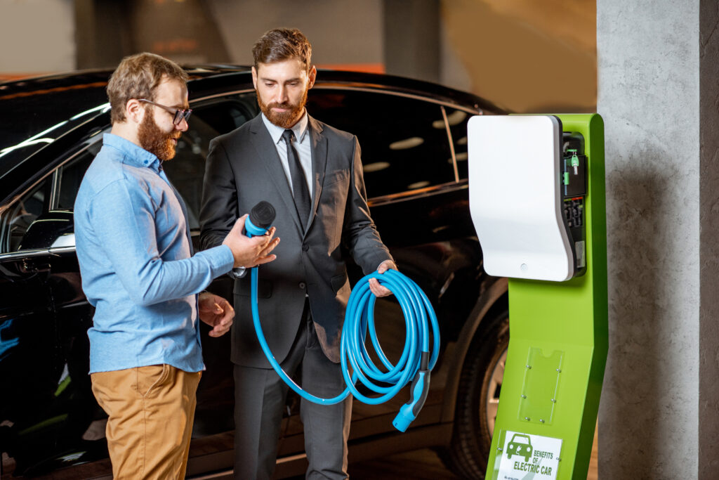 Customer with a sales consultant choosing a charging station for an electric car, standing with charging cable at a car dealership