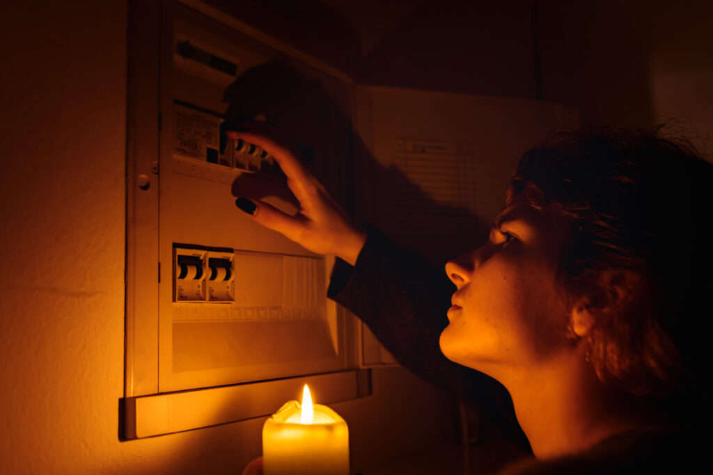 young woman with candles in complete darkness examines fuse box or electrical distribution board at home during power outage. Blackout, no electricity. Boca Electrical Services Boca Raton