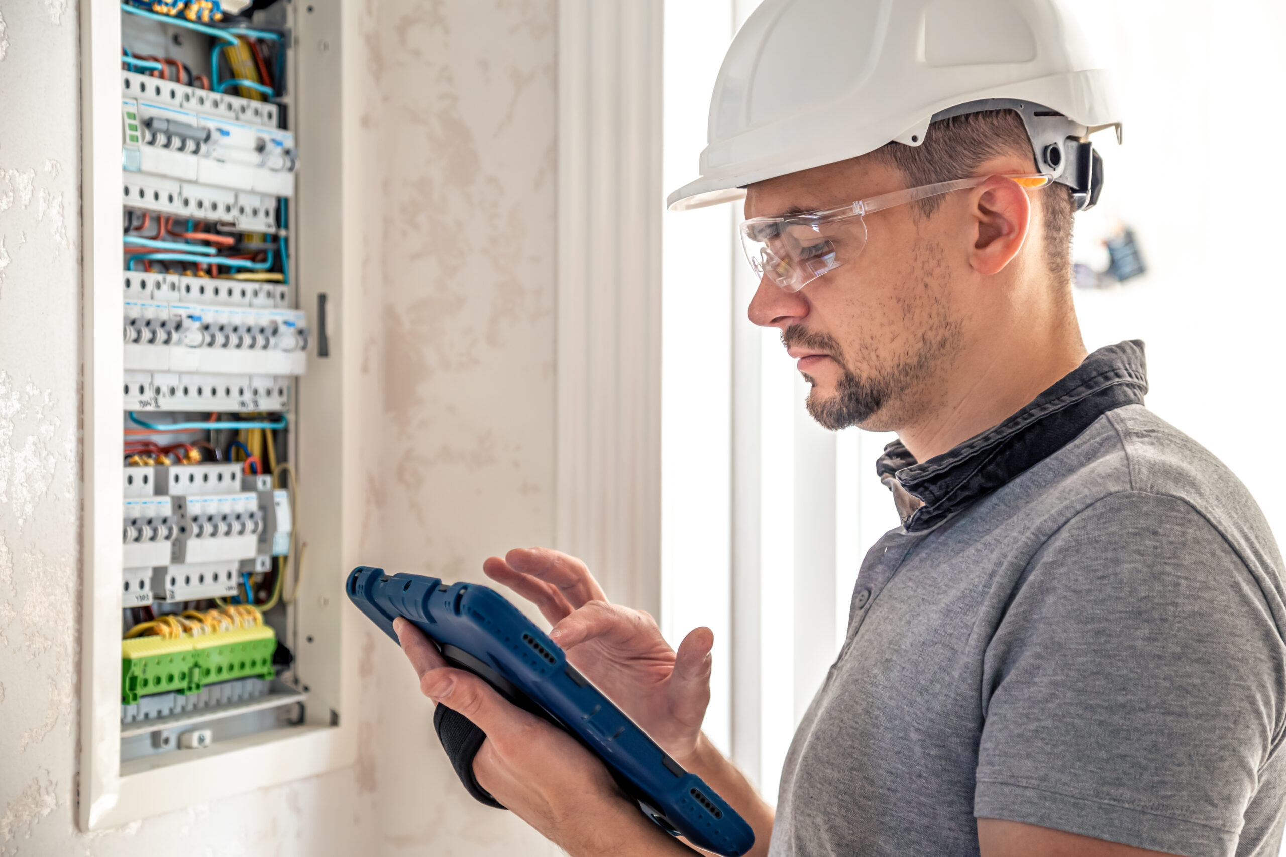 Man, an electrical technician working in a switchboard with fuses. Installation and connection of electrical equipment. Professional uses a tablet.