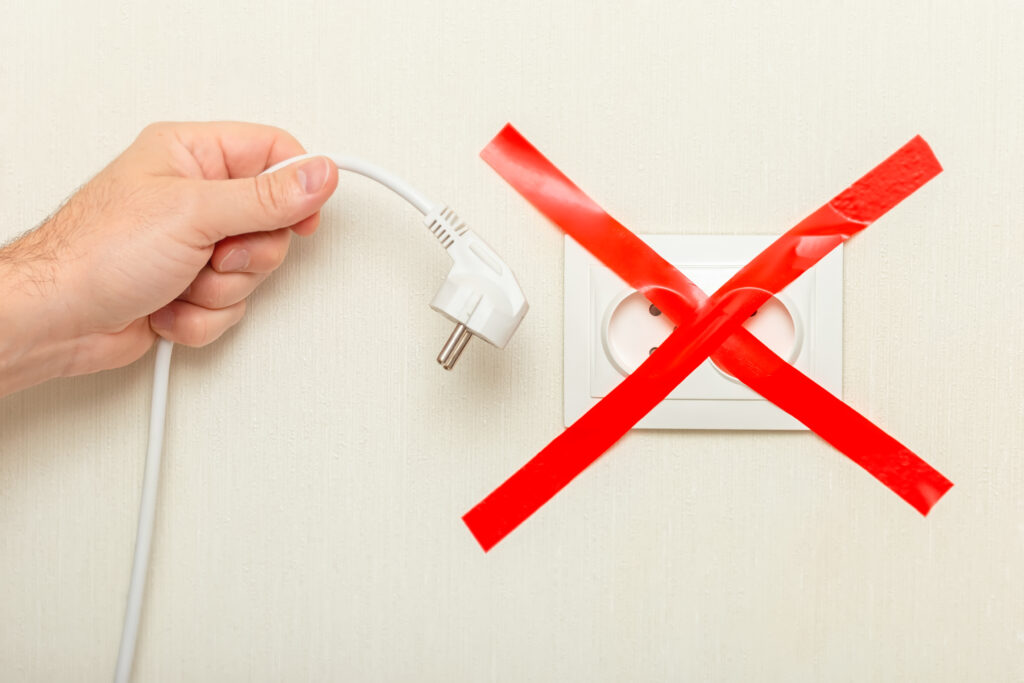 A mans hand holds a drooping white cord with a plug near an electrical outlet, tied with a red ribbon crosswise. 