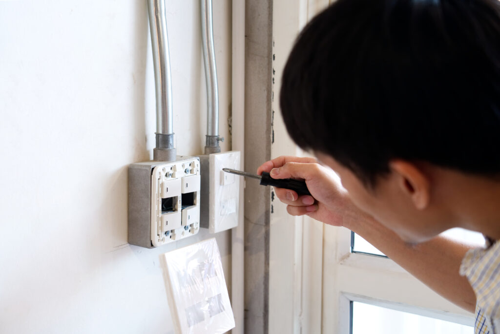 A Man fixing electrical system at wall by remove the switch mask. He using screw driver to loosening the screw to see inside what cause the system fail. DIY at home concept.