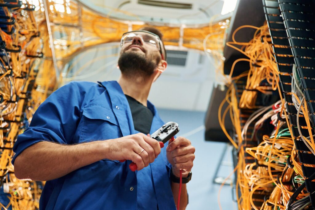 Busy by cutting the wire. Young man is working with internet equipment in server room.