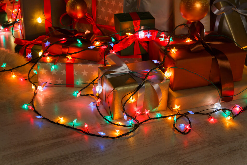 Wrapped present boxes decorated with red ribbon laying on the floor decorated with shining christmas led lights garland. Holiday evening decorations