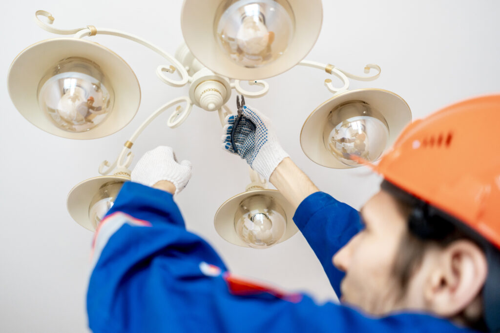 worker in uniform standing on the ladder and repair the chandelier at home