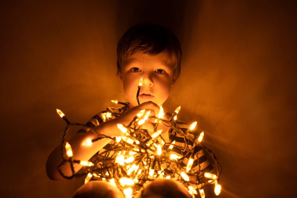 Babyboy play with christmas garland in dark. New year and christmas portrait, at home.